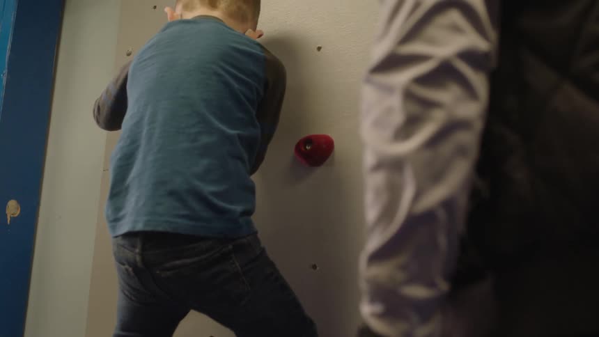 Man watches child climb up inside climbing wall