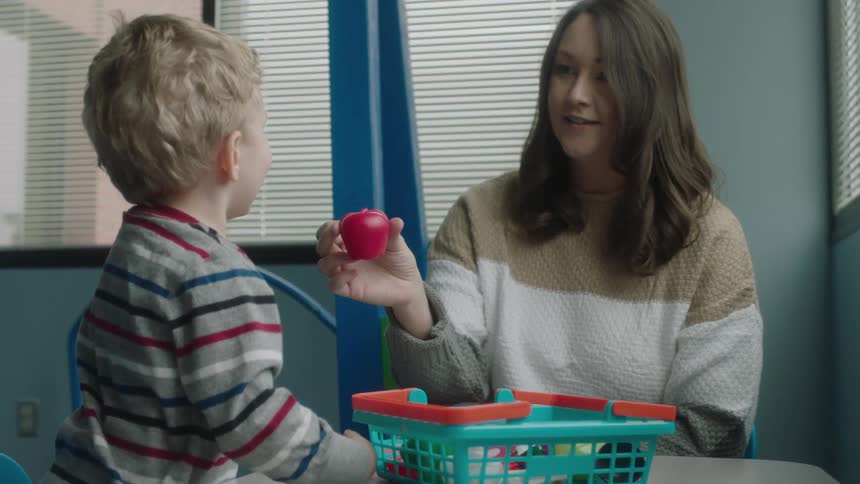A woman and a boy in a room sitting at a table playing with toys