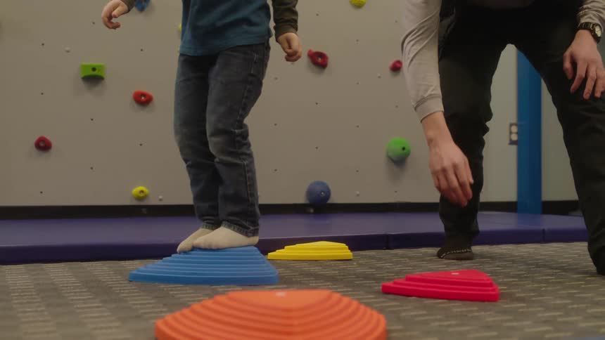 Father teaching his son to walk across colored paddings on a floor indoors