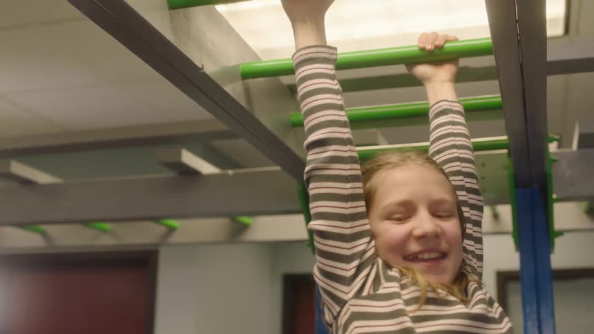 A girl in a room playing on monkey bars with a wall and doors in the background