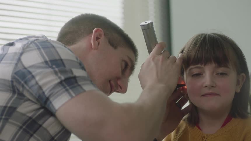 A doctor in a clinic looks inside a young girls ears