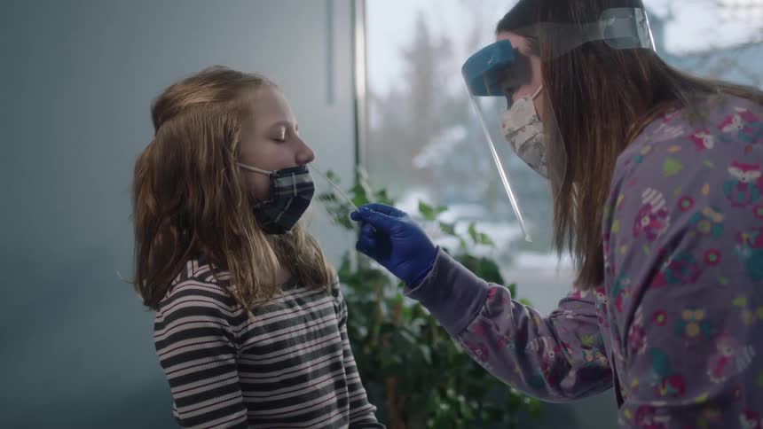 A girl and a nurse with masks in a clinic with the nurse putting a cotton swab and the girls nose