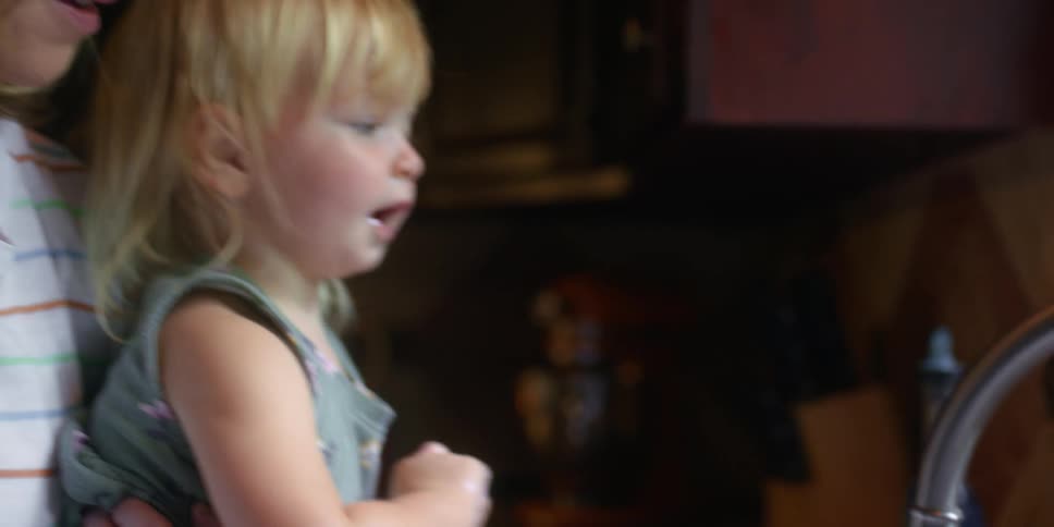 Blonde grandmother with glasses holding granddaughter wash their hands in the kitchen