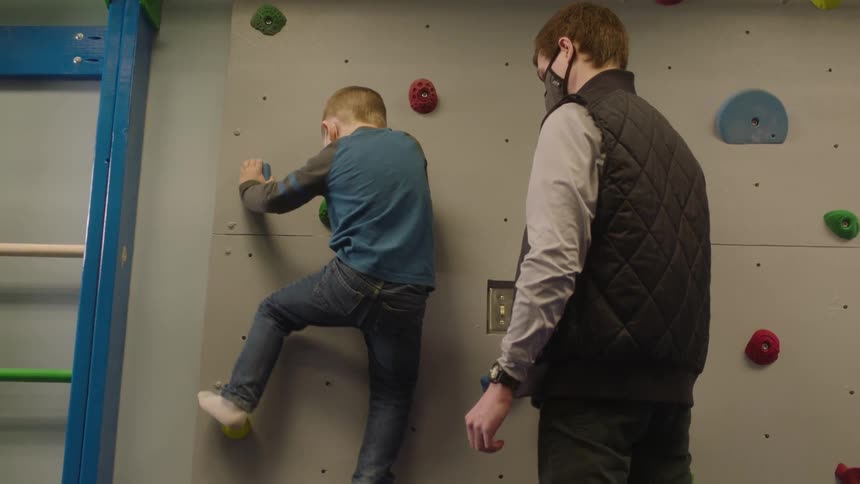A father watches as his son makes his way up a climbing wall