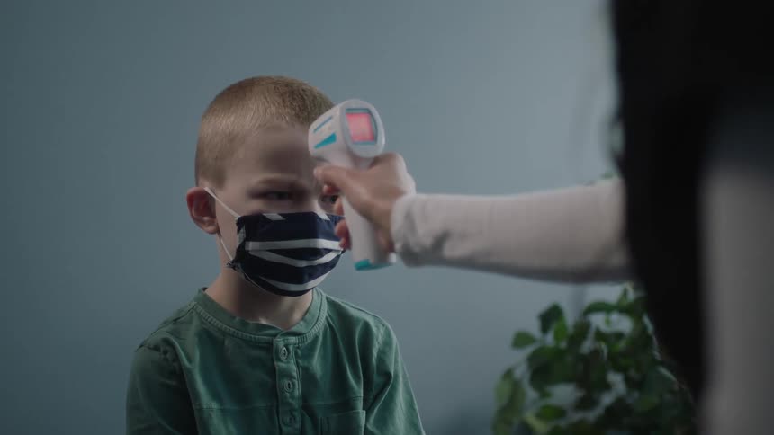 A nurse takes a young boys temperature as he sits in a doctors office