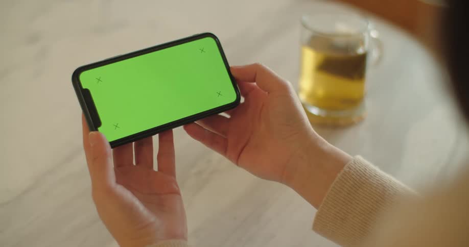 Woman sits at table near tea mug viewing mobile phone