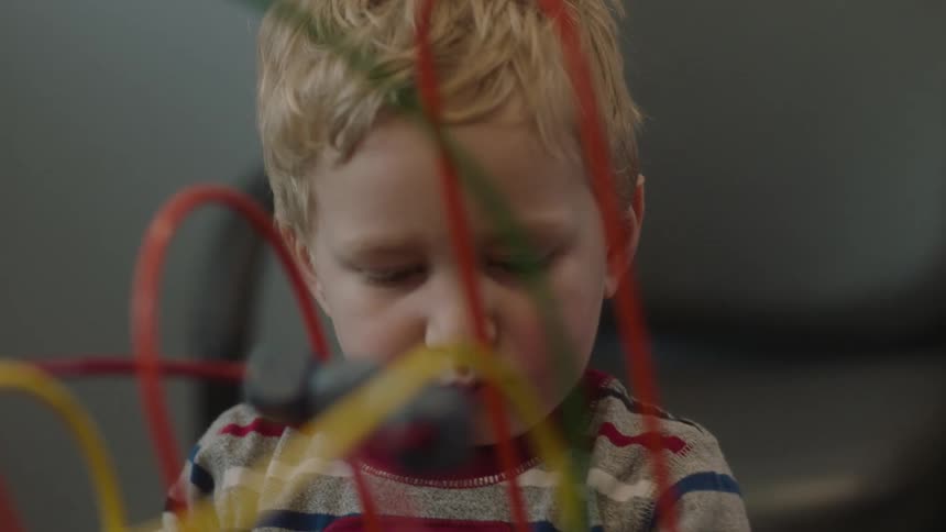 A little blond boy is playing with a toy that has moving pieces