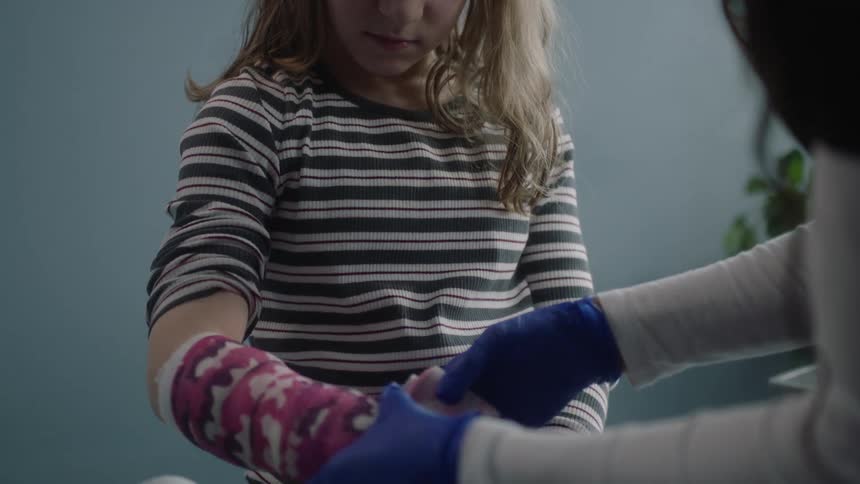 A medical person wraps printed tape around a girls arm for her cast
