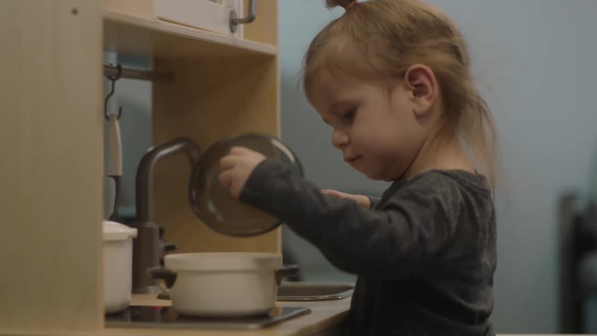 A girl in a room playing with a toy stove and sink with a wall in the background