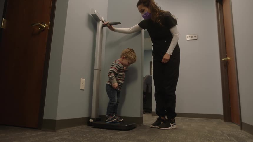 A nurse has a toddler boy step on the scale and lower the height adjustment in a doctor office