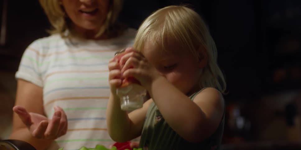 A grandmother is standing next to a small girl who is shaking a spice into something unseen