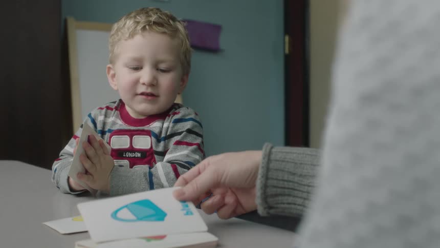 A young boy is shown cards with various pictures on them by an adult female