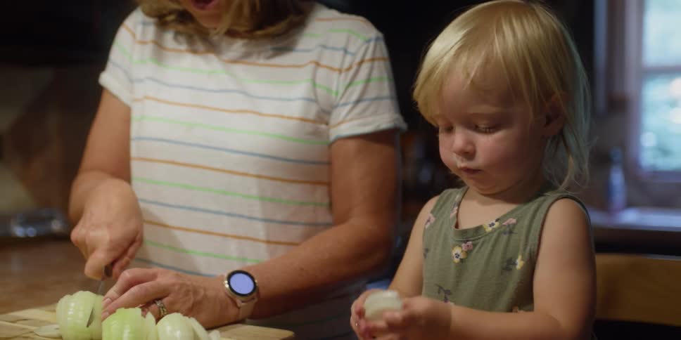A toddler helps her mom separate sliced onions for cooking