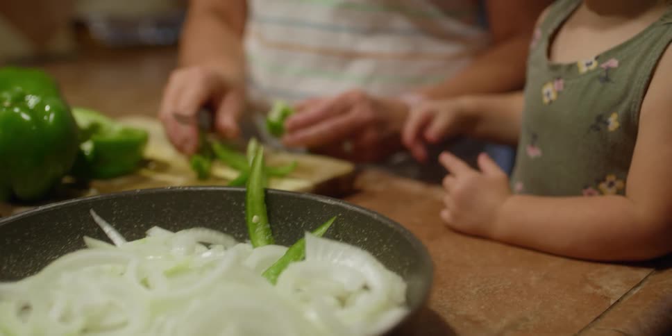 An elderly lady cuts vegetables as a little girl places them on a plate