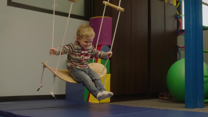A child is smiling as he is riding a swing in a play room