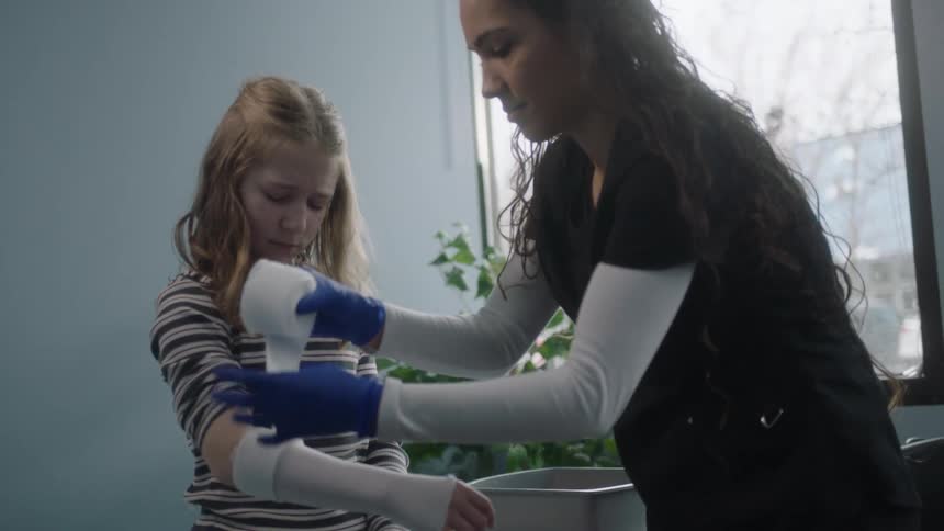 A nurse wraps a girls arm in gauze at a doctors office