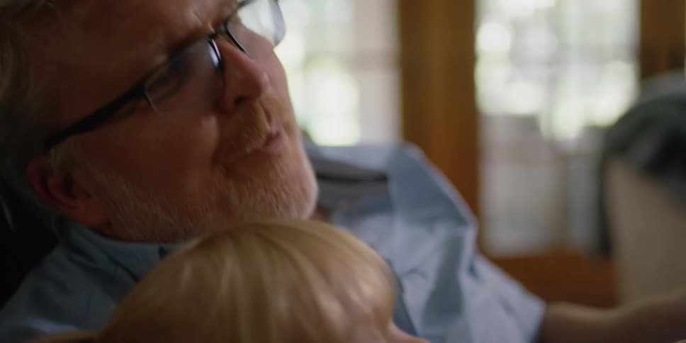 An elderly man is reading to a child as they rock