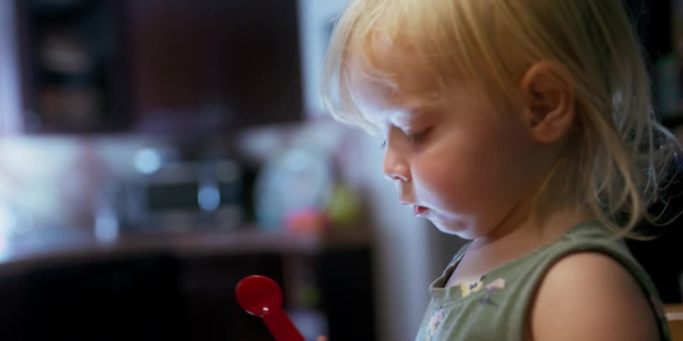 A toddler plays with measuring spoons and cups in the kitchen