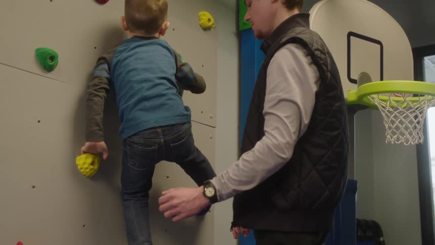 A father stands by and guides his son as he climbs up a rock wall