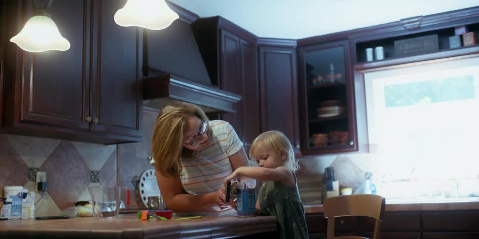 A woman and a small child are in a kitchen opening a can with a can opener