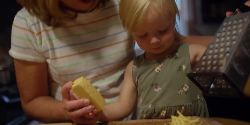 Mother and daughter grate cheese together smiling