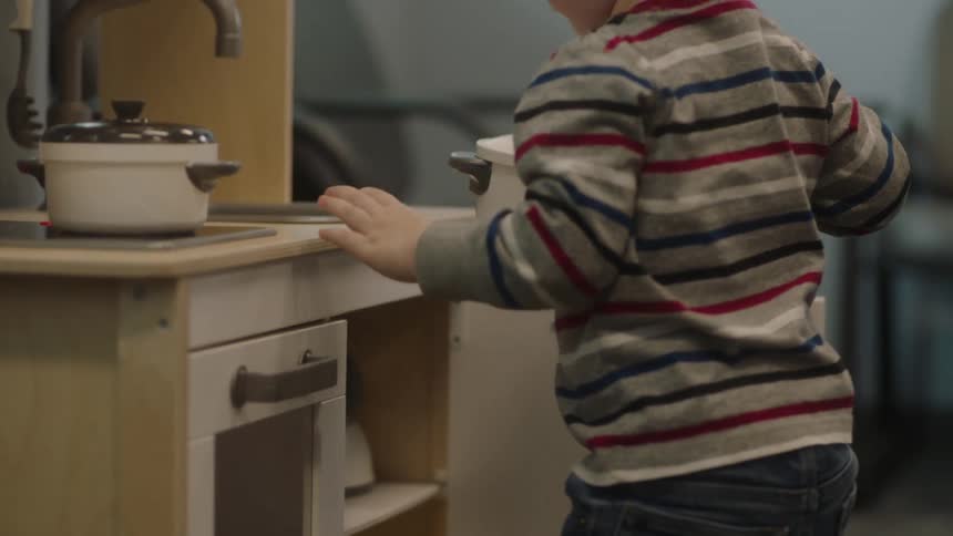 A toddler boy plays with a toy kitchen and toy pots