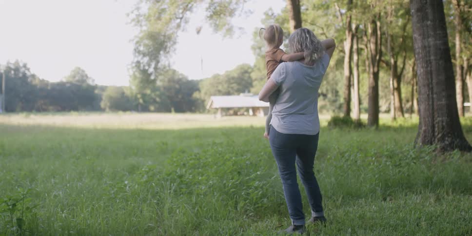 A woman holding a little girl with trees the sky and clouds in the background