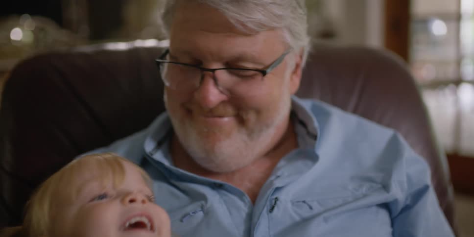 A little girl sits on her grandfathers knee as he reads a book to her