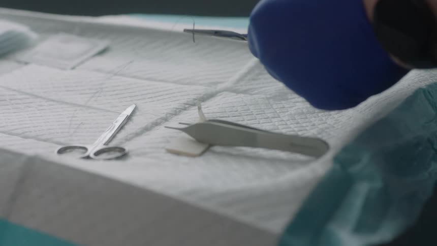 A person with gloves in a room picking up surgical tools