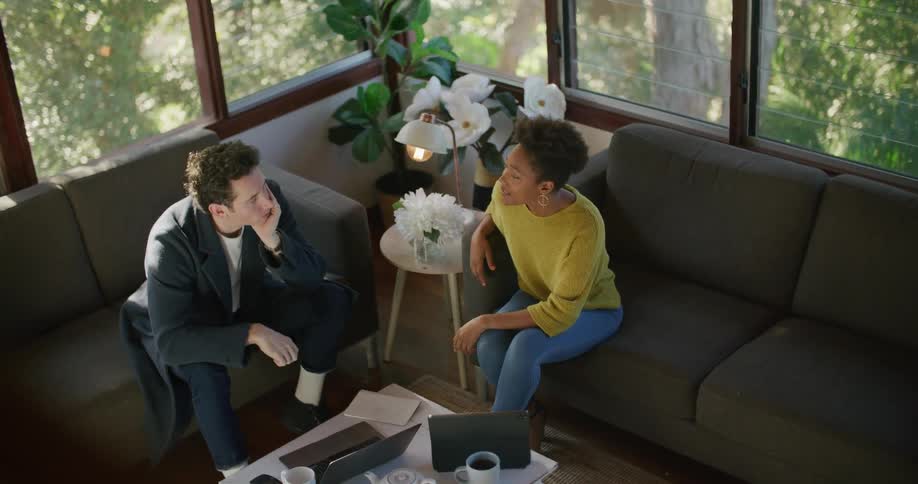 Woman in yellow sweater and jeans sits on sofa with man with black jacket and pants and talk to each other in the living room