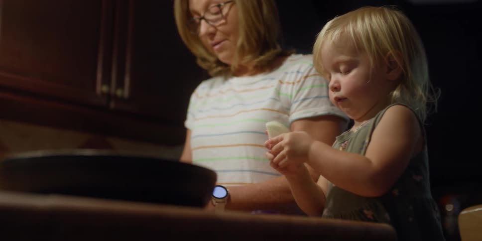 An elderly lady cuts vegetables as a small child places it on a plate