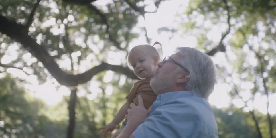 Grandpa picks up his granddaughter as she points at the trees in the yard
