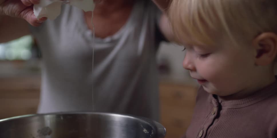 A woman and a girl in a kitchen with the woman cracking an egg into a bowl