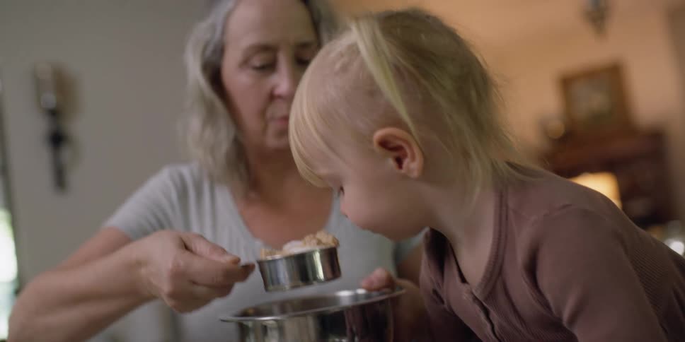 A woman and child pour ingredients in a mixing bowl