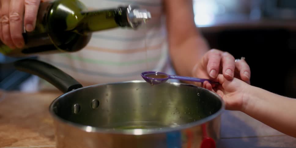 A mother and daughter putting olive oil into a pot