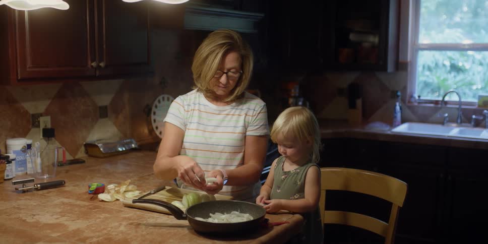 A woman and a girl in a kitchen putting vegetables in a pan