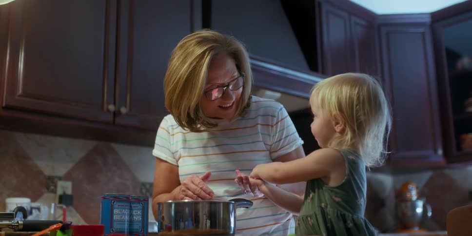 A woman plays a hand game with a small female child in a kitchen near the stove