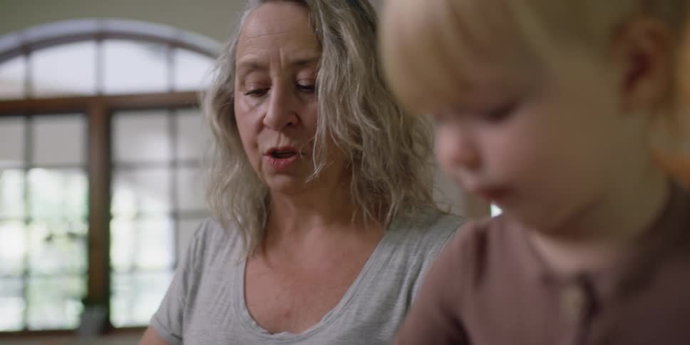 A grandmother and her toddler granddaughter are in the kitchen talking