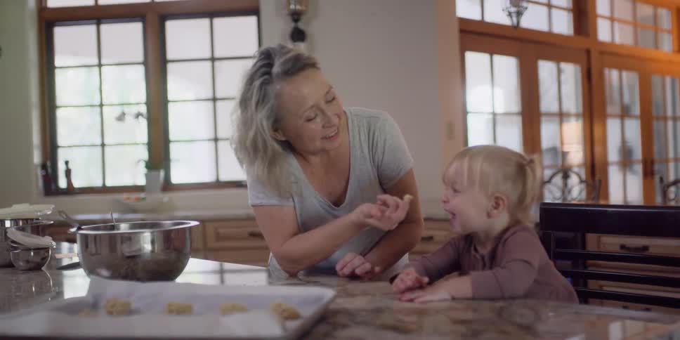 A woman and a girl in a kitchen with a wall and window in the background