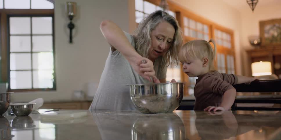 A woman is talking to a child as she mixes something in a large bowl