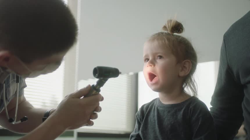 A medical person uses a light to look inside a toddler girls mouth