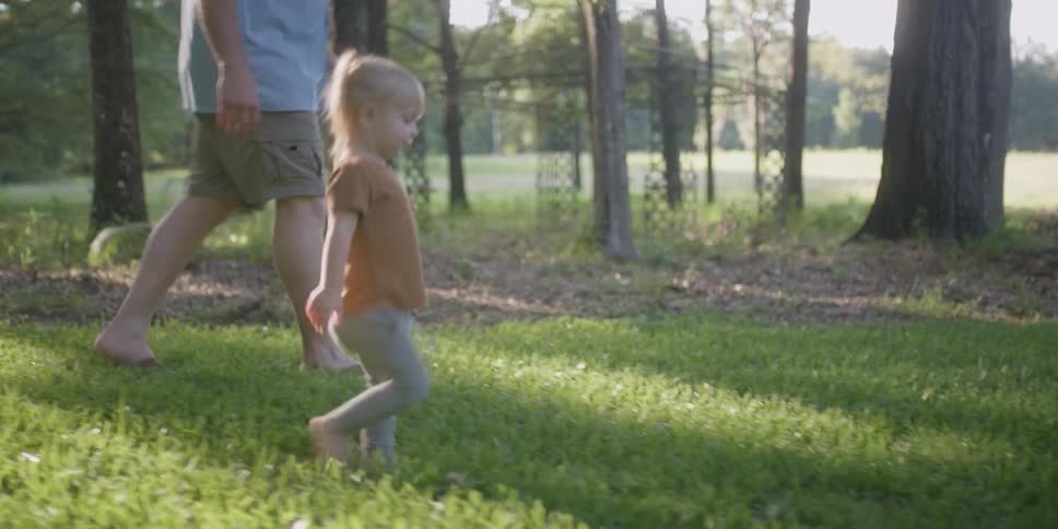 An older grey haired man walks with a small girl through a forest area near a path