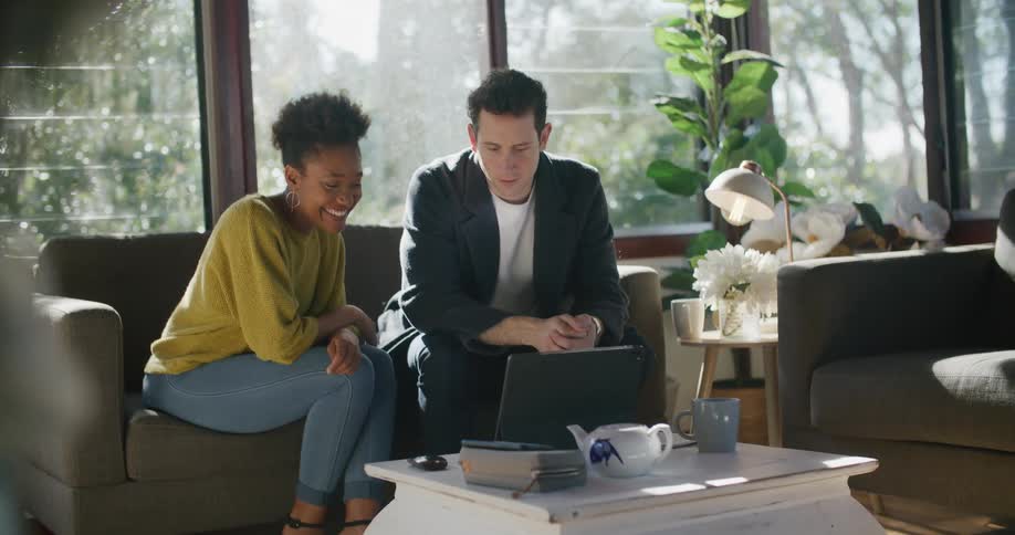 Man and woman sit on couch talking to someone via laptop