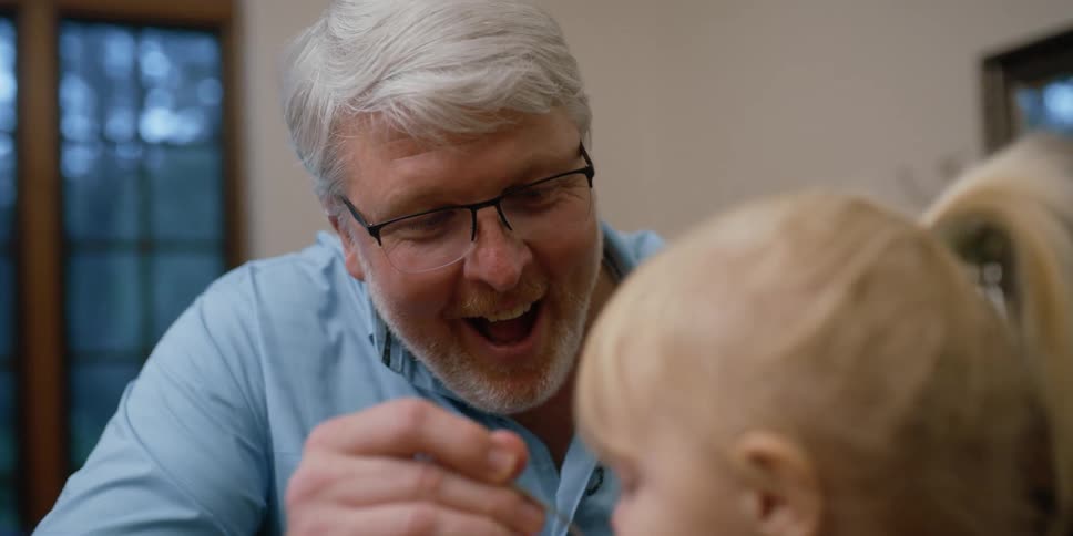 An older man feeds a toddler girl from a small bowl