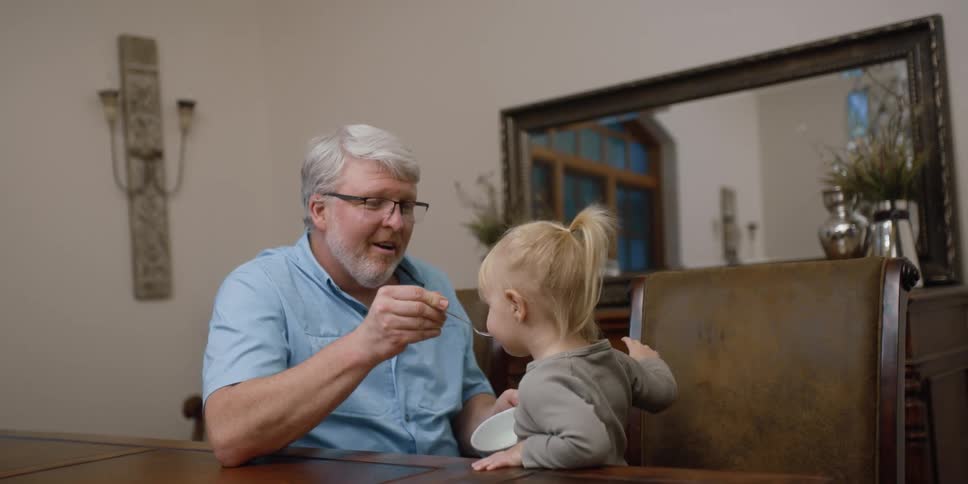 A man feeds a toddler girl something from a bowl