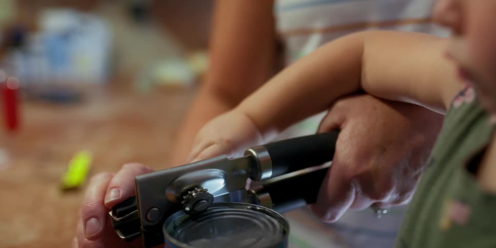 Grandmother helps little granddaughter open a can in the kitchen