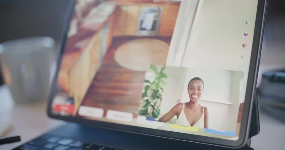 Finger touches a photo of a kitchen on a laptop while a black woman smiles talks and waves in the lower right corner of the screen