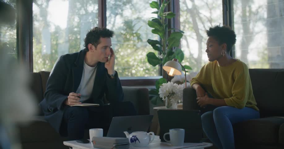 A man takes notes while interviewing a woman in a house