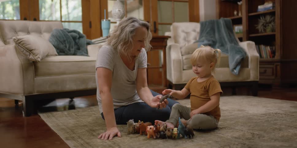 A woman sits on the floor playing with her toddler granddaughter