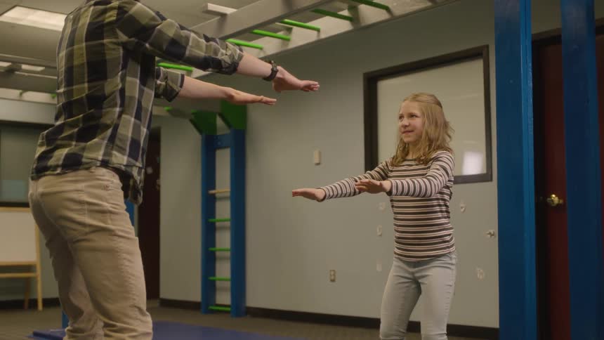 Man with plaid shirt and beige pants exercises with blonde girl